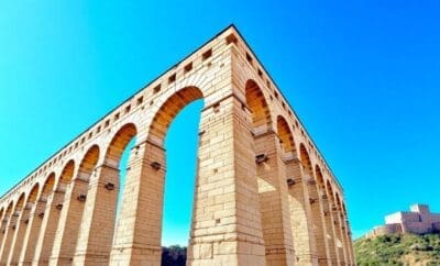 Segovia's Roman aqueduct and distant castle under a blue sky.